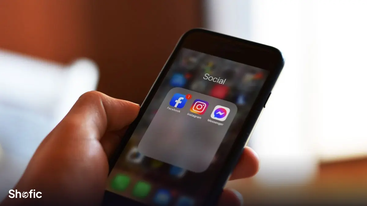 A hand holding a phone showing social media apps