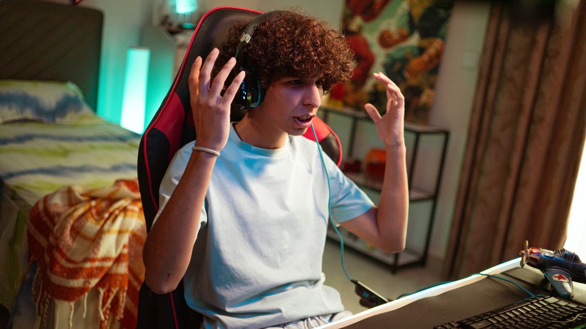 A gamer streaming live on Twitch at a purple-lit desk setup with a microphone and dual monitors